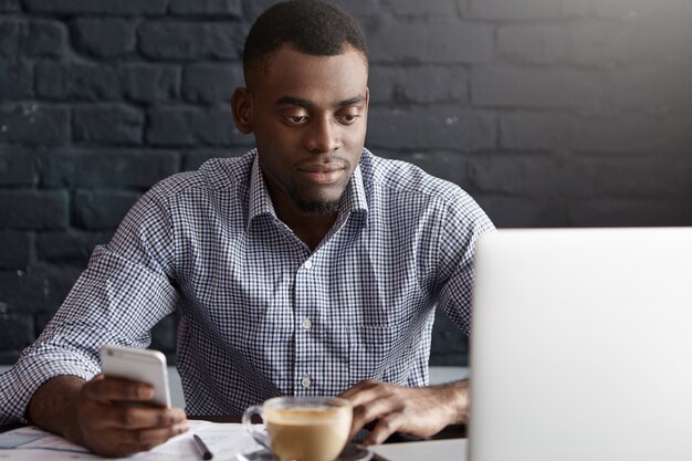 Handsome young African man in formal shirt surfing internet on mobile phone