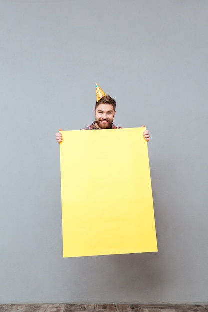 Handsome young bearded birthday man holding blank board jumping