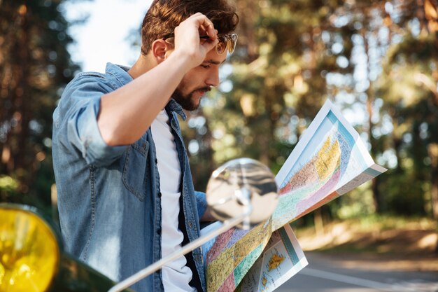 Handsome young bearded man near scooter looking at map