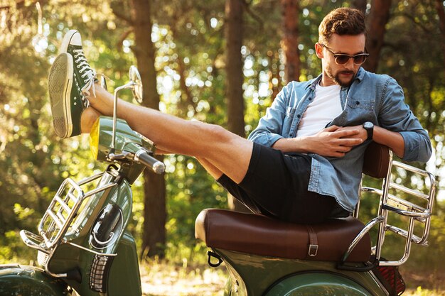 Handsome young bearded man sitting on scooter outdoors