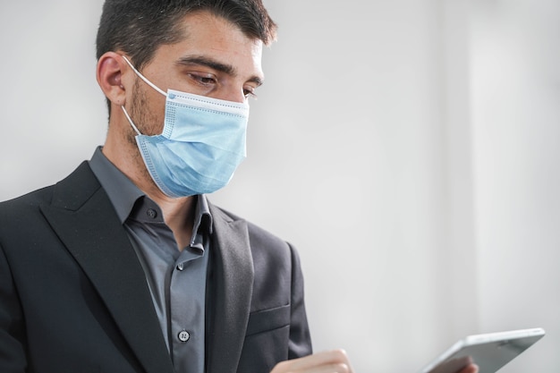 Handsome young business man wearing protective mask working with tablet in a white background