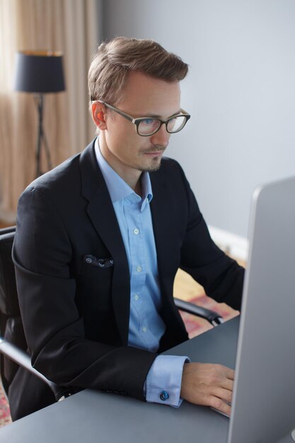 オフィスでコンピューターを使用して作業しているハンサムな若いビジネスマン。