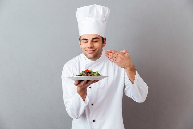 Handsome young cook in uniform smell salad