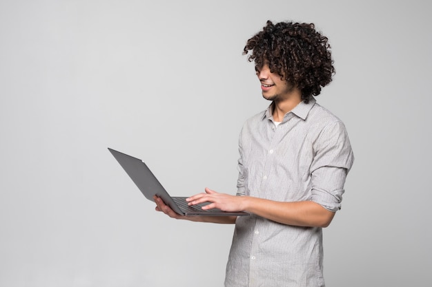 Free photo handsome young curly haired man working on laptop computer standing of isolated on white wall,