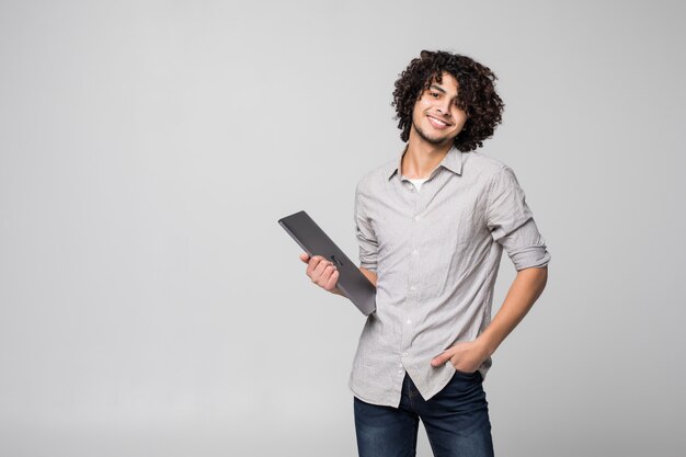 Handsome young curly haired man working on laptop computer standing of isolated on white wall,