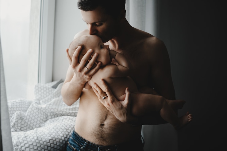 Free Photo handsome young dad holds newborn baby close to his heart standing before a bright window