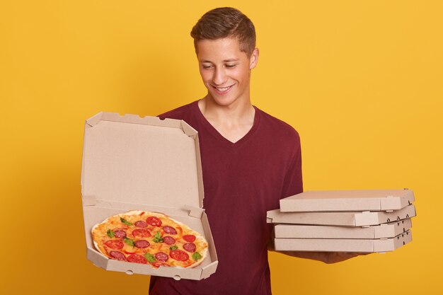 Handsome young delivery worker dresses burgundy casual t shirt holding pizza in boxes