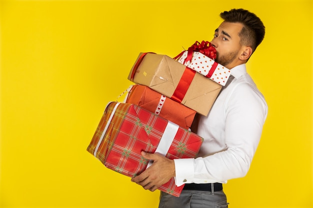 Handsome young european guy is holding heavy packed gifts and presents