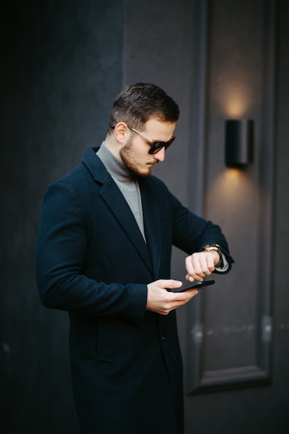 Foto gratuita bello giovane modello di moda in posa sulle strade della città. ritratto di moda all'aperto, uomo elegante in cappotto elegante.