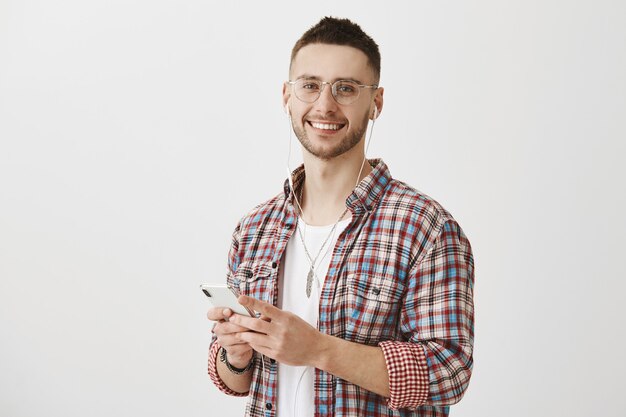 Handsome young guy with glasses posing with his phone and earphones