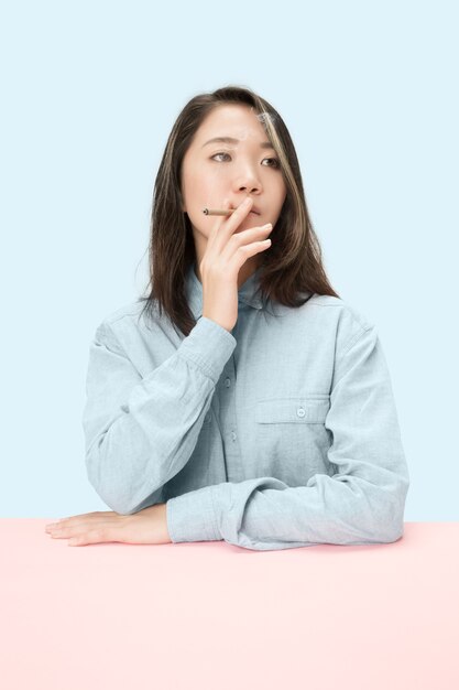 Handsome young korean women smoking cigar while sitting at table at studio.