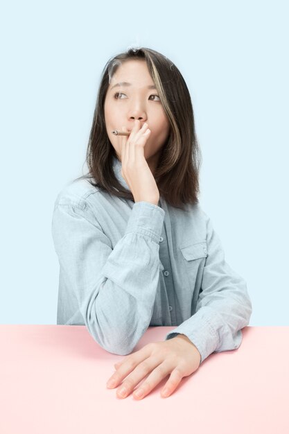 スタジオでテーブルに座っている間葉巻を吸っているハンサムな若い韓国人女性。