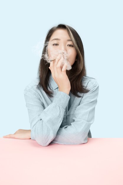 Handsome young korean women smoking cigar while sitting at table at studio.