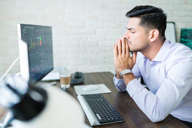 Handsome young Latin finance professional sitting with eyes closed while hoping for good stock trade while working at home