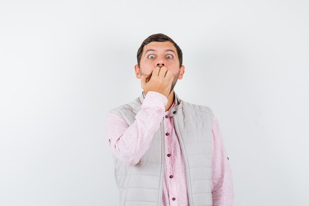 Handsome young male biting nails emotionally in shirt, vest and looking scared. front view.