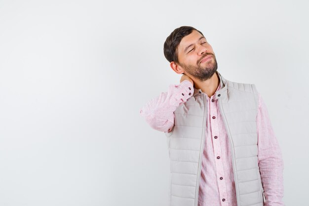 Handsome young male keeping hand on neck in shirt, vest and looking relaxed. front view.