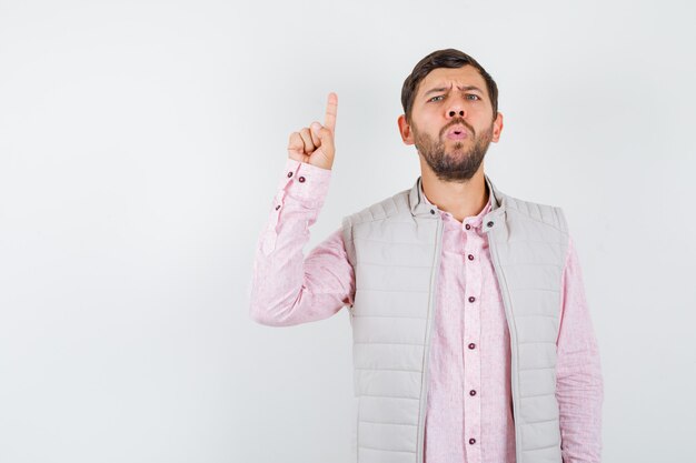 Handsome young male pointing up in shirt, vest and looking pensive , front view.