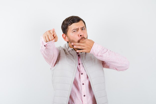 Handsome young male in shirt, vest pointing at front, whistling with fingers and looking confident , front view.