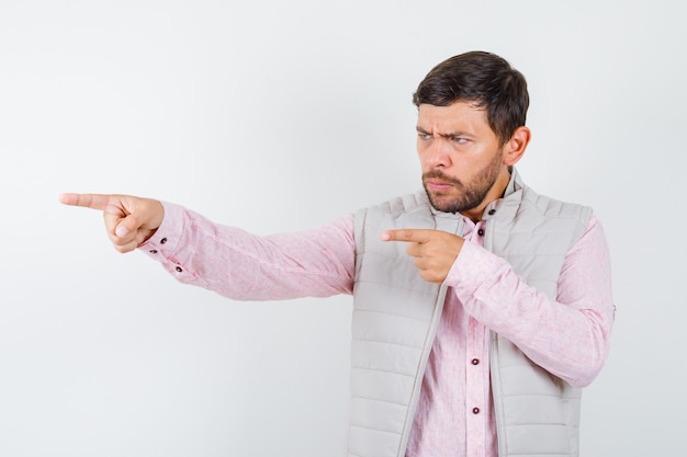 Bel giovane maschio in camicia, gilet che punta da qualche parte e sembra concentrato, vista frontale.