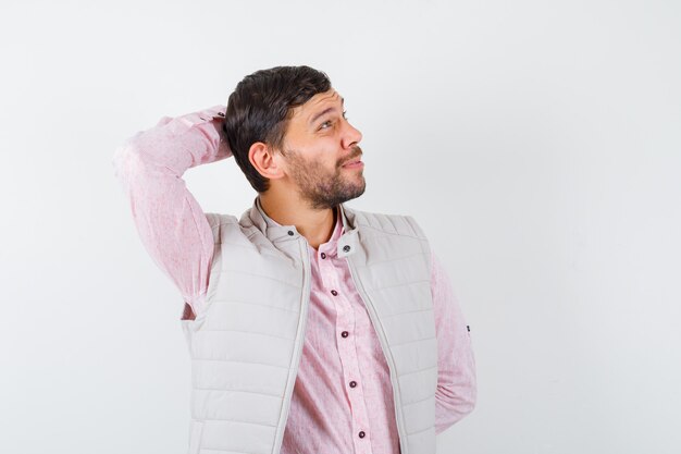 Handsome young male in shirt, vest with hand behind head and looking pensive , front view.