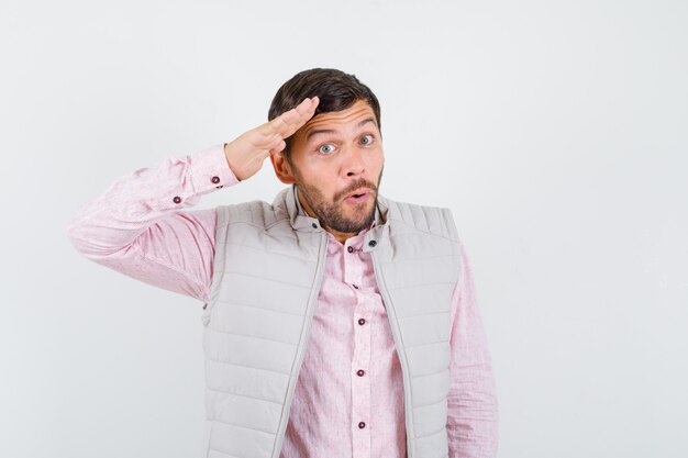 Handsome young male showing salute gesture in shirt, vest and looking wondered. front view.