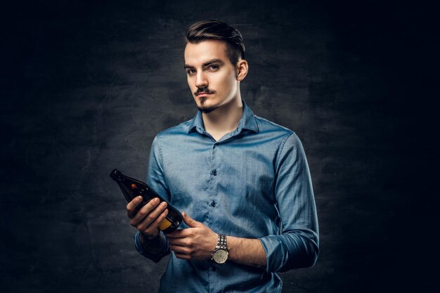 Handsome young male with a tattoo on his arm holds craft bottled beer.