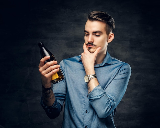 彼の腕に入れ墨を持つハンサムな若い男性は、クラフト瓶ビールを保持しています。