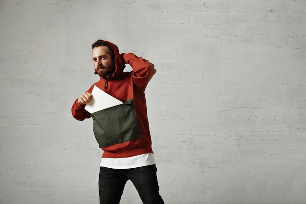 Free photo handsome young man adjusts the hood of his stylish anorak and takes a blank piece of paper out of its front pocket