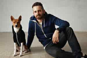 Free photo a handsome young man and a brown and white dog wearing matching dark hoodies isolated on white