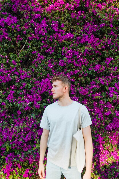 Мешок ткани нося красивого молодого человека стоя около розового дерева цветка