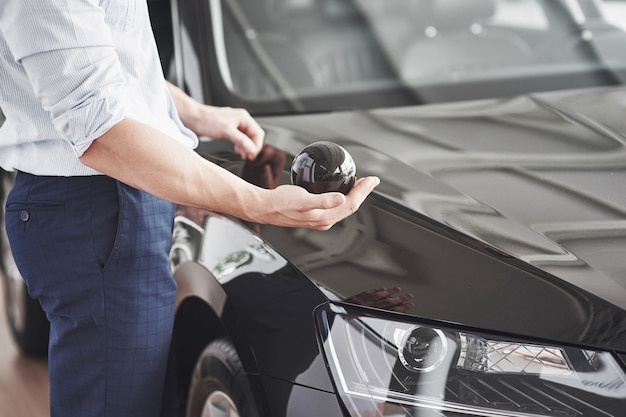 車の近くに立っているカーサロンでハンサムな若い男のコンサルタント。