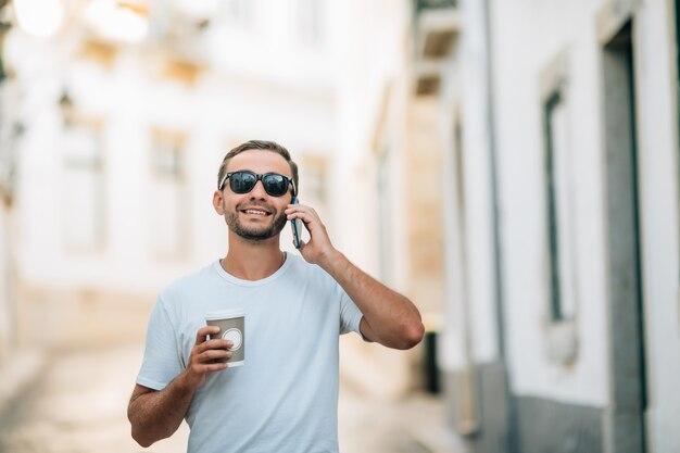 電話で会話をしている街の通りで流行の服を着たハンサムな若い男