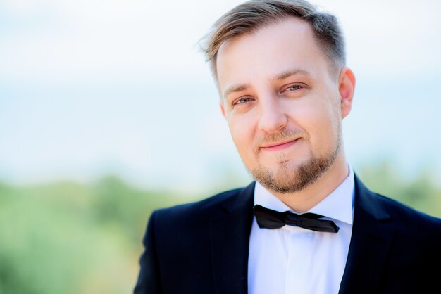 handsome young man in festive suit and black bow tie stands before a great sea view