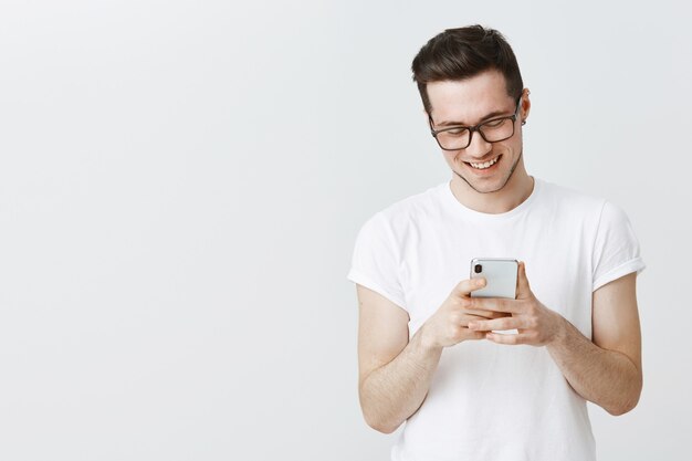 Красивый молодой человек в очках с помощью мобильного телефона