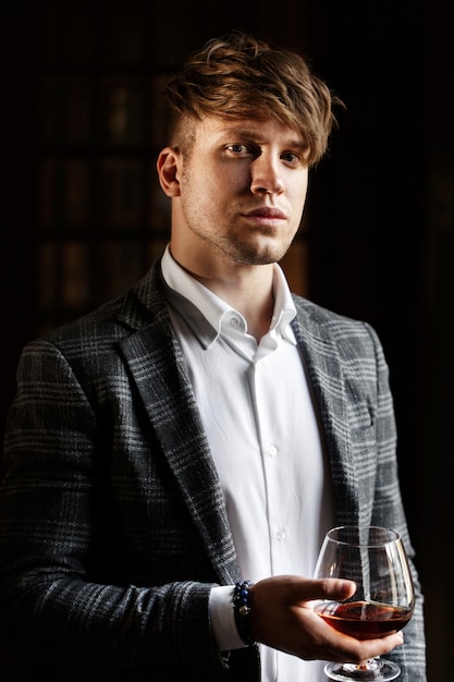 Handsome young man in grey suit stands with a glass of whisky