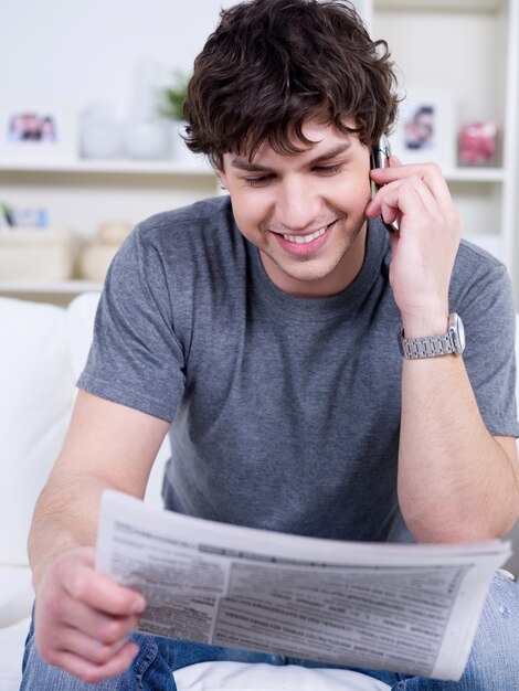 ハンサムな若い男が自宅で電話で話し、新聞を読む