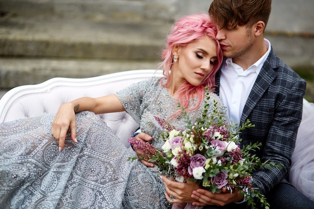 Красивый молодой человек обнимает нежная женщина с розовыми волосами, сидя на белом диване