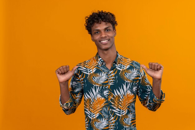 Handsome young man in leaves printed shirt pointing thumb finger at himself 