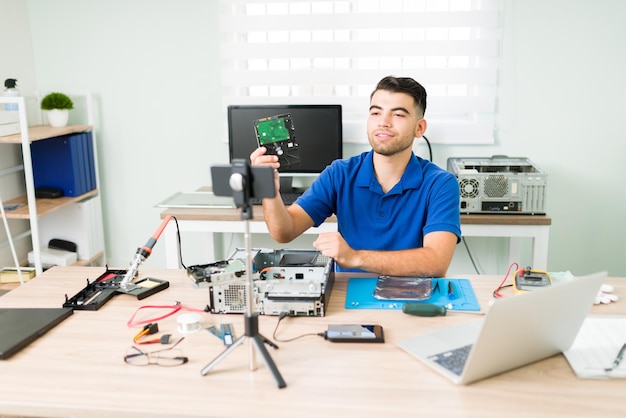 Foto gratuita bel giovane live streaming di un tutorial tecnico con uno smartphone. tecnico informatico che registra un video per i suoi seguaci e mostra un disco rigido