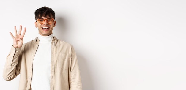 Free photo handsome young man making order showing number four fingers and smiling standing on white background