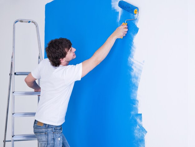 Handsome young man painting the wall in blue