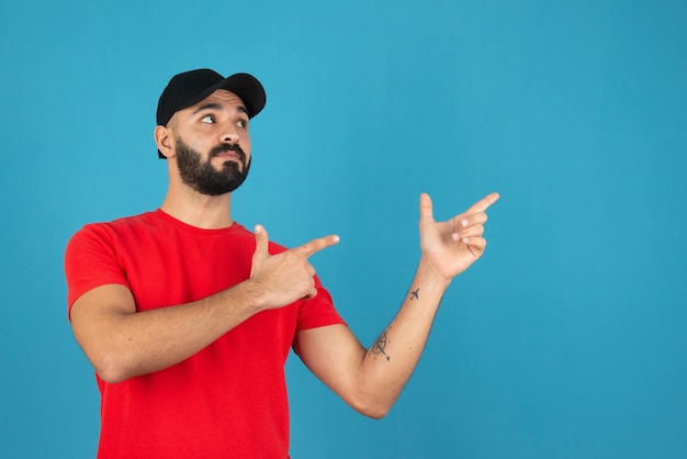 Handsome young man pointing away against blue wall . 