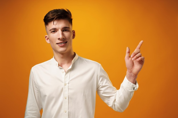 Handsome young man pointing copy space against yellow background