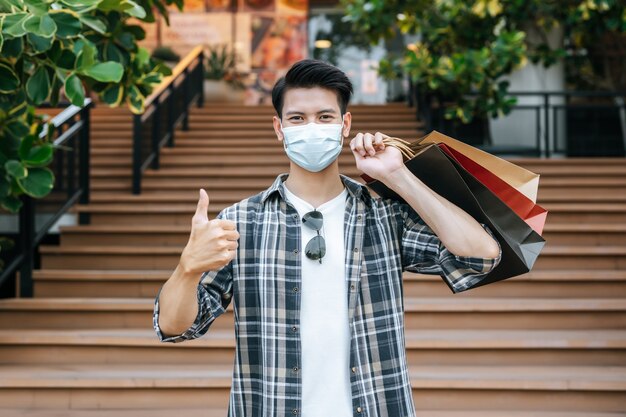 Handsome young man in protection mask holds multiple paper bag