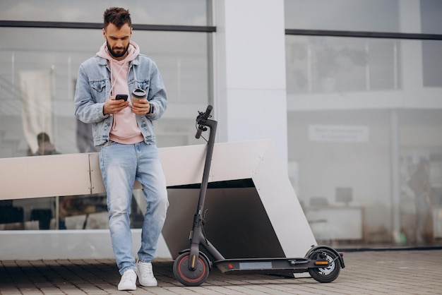 Handsome young man riding electric scooter using phone and drinking coffee