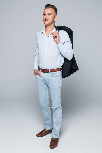 Handsome young man in shirt and jeans hold his jacket on the shoulder isolated on light grey wall