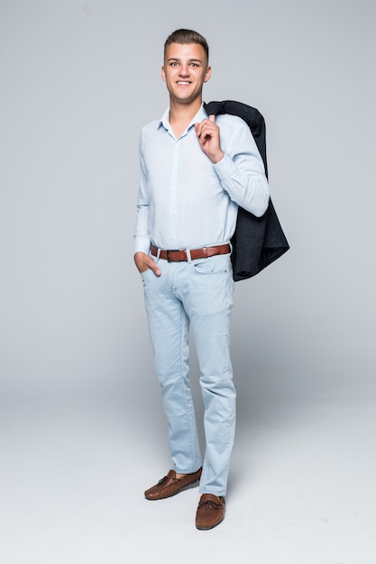 Handsome young man in shirt and jeans hold his jacket on the shoulder isolated on light grey wall