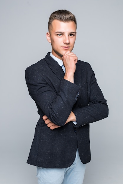 Handsome young man in shirt and jeans holds his arm under his chin isolated on white