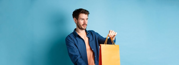 Free photo handsome young man shopping salesman stretching out orange shopping bag to client looking aside stan