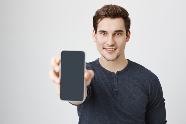 Красивый молодой человек показывает дисплей мобильного телефона